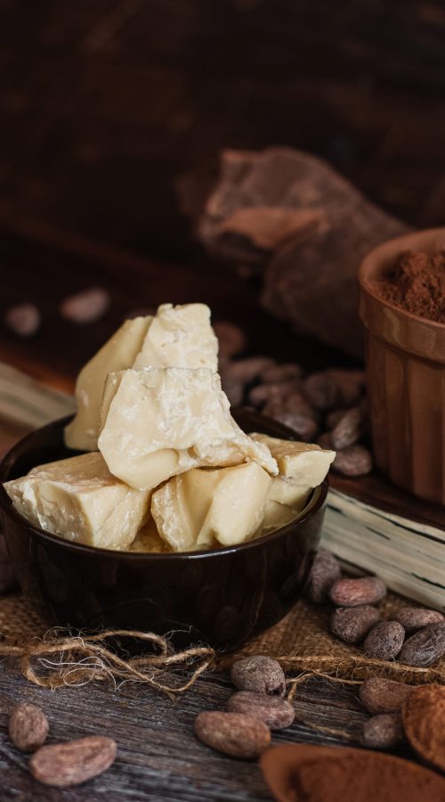 Unsweetened baking block chocolate, cocoa powder, cocoa butter and cocoa beans on old wooden background.